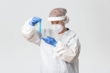 Tıp çalışanları, covid-19 salgını, koronavirüs konsepti. Kişisel koruyucu ekipmanlı dikkatli görünümlü kadın doktorun portresi test tüpünde aşı tutuyordu, virüsün tedavisini buldu.