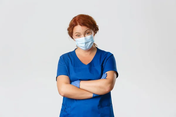 Medical workers, covid-19 pandemic, coronavirus concept. Skeptical and judgemental, serious-looking female doctor, physician cross arms and raise eyebrows with skepticism, wear face mask and gloves