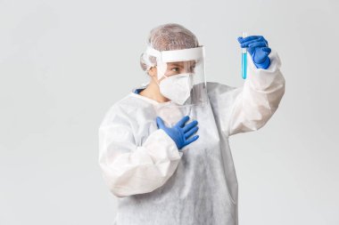 Tıp çalışanları, covid-19 salgını, koronavirüs konsepti. Şaşırmış ve heyecanlı kadın doktor, teknoloji laboratuvarı ya da bilim adamı aşı umuduyla test tüpüne bakıyor, virüsün tedavisini buldu, gri arka plan