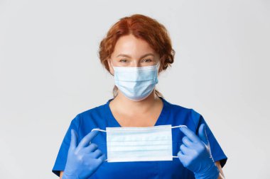 Tıp çalışanları, covid-19 salgını, koronavirüs konsepti. Gülümseyen dost canlısı bayan doktor, doktor yüz maskesi nasıl takılır, lastik eldivenle nasıl tutulur?