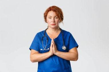 Tıp, sağlık ve koronavirüs konsepti. Ciddi görünümlü bir sağlık çalışanı, salgın sırasında evde kalmak için yalvarıyor ve sosyal mesafeyi korumak için gri arka plan için dua ediyor.