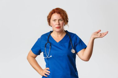 Tıp, sağlık ve koronavirüs konsepti. Hüsrana uğramış ve rahatsız olmuş kızıl saçlı kadın doktor, kafası karışmış ve kızgın görünen doktor, korkuyla el kaldırıyor, bu jest de ne?