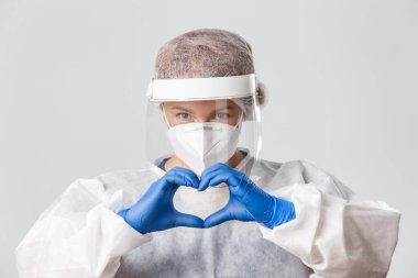 Tıp çalışanları, covid-19 salgını, koronavirüs konsepti. Kişisel koruyucu ekipmanlı, şefkatli ve kendini işine adamış bir kadın doktor kalp jestini desteklerken dikkatli olun.