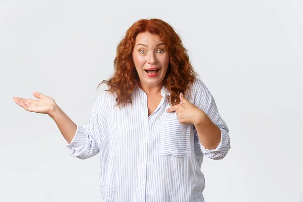 Confused and surprised middle-aged woman react to nonsense accusations, pointing at herself and raise hand sideways clueless, standing puzzled over white background — Stock Photo, Image