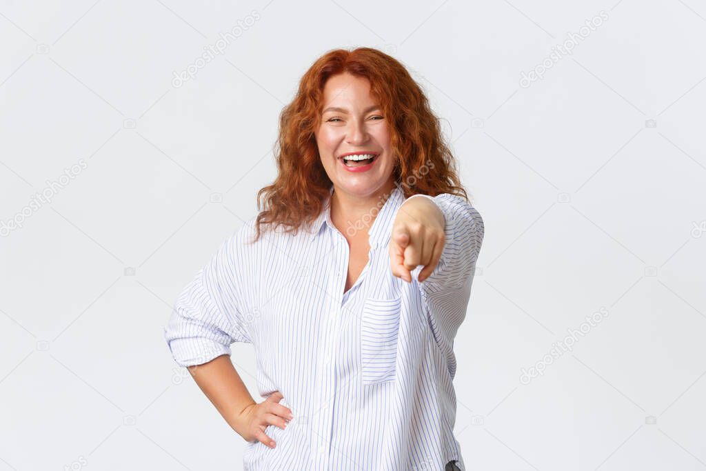 Concept of congratulation and praises. Portrait of cheerful, laughing and smiling cute middle-aged redhead woman pointing finger at camera, adult female choosing you, white background