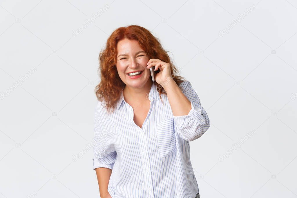 Portrait of cheerful, beautiful middle-aged redhead woman talking on phone, holding smartphone and looking happy while having conversation, good cellphone receptions, cellular service