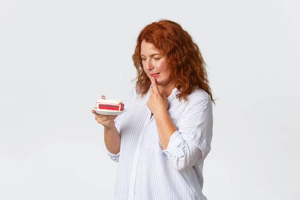 stock image Holidays, emotions and lifestyle concept. Indecisive cute middle-aged female with red hair making decision, wanting to eat cake but worry about calories, looking throughful at dessert