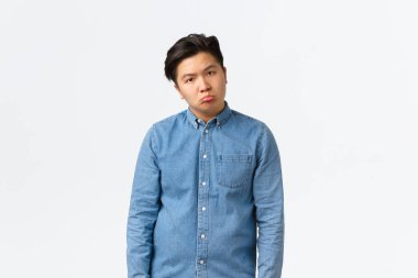 Hüzünlü ve üzgün Asyalı adam depresif görünüyor, kameraya somurtuyor ve somurtuyor, dikkatsiz ve sıkıntılı hissediyor, uzun vardiyadan sonra tükenmiş, beyaz arka plan üzerinde duruyor,