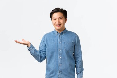 Gülümseyen genç girişimci kendi işini kuruyor, bir şeyler gösteriyor, ürünü elde gösteriyor, sol kolu işaret ediyor, beyaz arkaplan üzerinde nesne veya bağlantı kuruyor