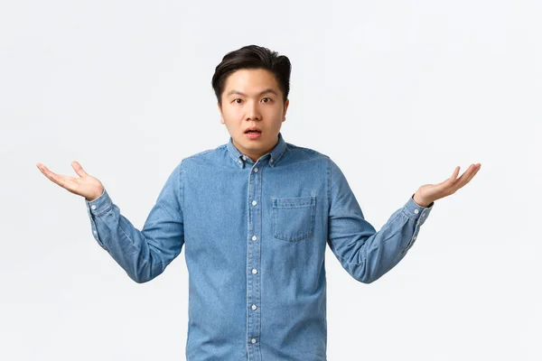 Förvirrad och förbryllad asiatisk man i skjorta kan inte förstå vad som händer, lyfta händerna i sidled och rycka, väntar förklaring, undrar, stående ifrågasatt vit bakgrund — Stockfoto