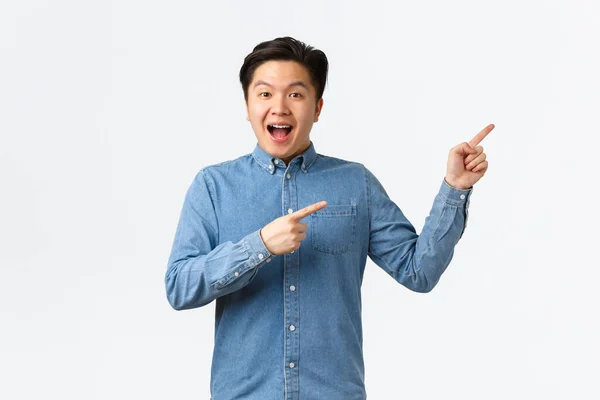 Excited and happy asian man making big announcement. Guy with braces smiling amused and pointing fingers upper right corner. Male student showing courses or online link, white background — Stock Photo, Image