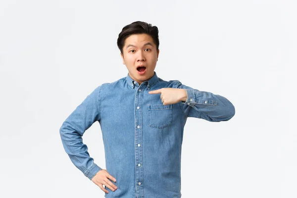 Überrascht und befragt asiatischer gutaussehender Typ in blauem Hemd, der mit neugieriger Miene auf sich selbst zeigt, erwähnt oder genannt wird, aus der Menge ausgewählt, weißer Hintergrund stehend — Stockfoto