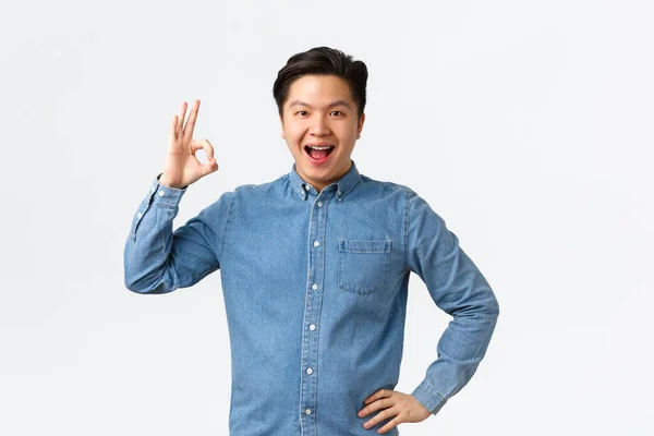Spokojenost sebevědomý usměvavý asijský chlap s rovnátka, ukazující v pořádku gesto, doporučit perfektní lékař klinika, skvělá stomatologie, být spokojen s výsledky, stojící bílé pozadí ohromen — Stock fotografie