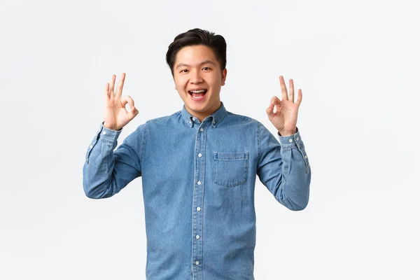 Usmívající se spokojený asijský muž s rovnátka v modré košili, ukazující v pořádku gesto, blahopřát osobě s vynikající práci, dobře provedeno, doporučit perfektní servis nebo kvalitu, bílé pozadí — Stock fotografie