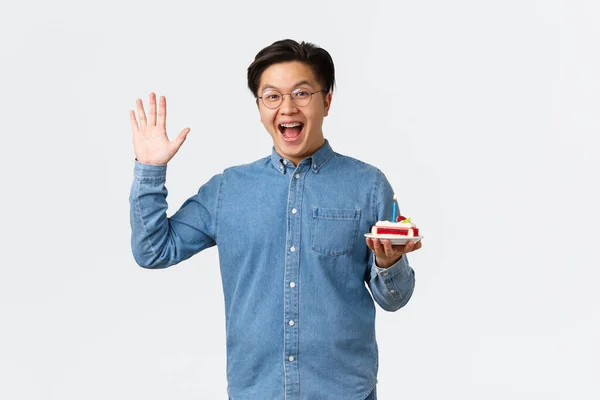 Celebration, holidays and lifestyle concept. Friendly happy guy waving hand to say hello and bring birthday cake to person celebrating, enjoying b-day party, standing upbeat white background