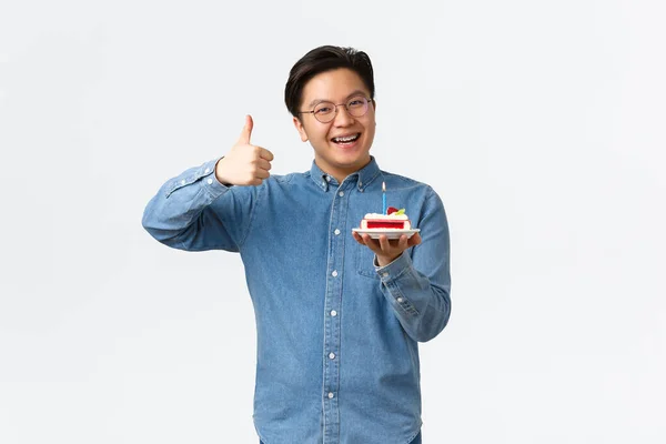 Oslava, dovolená a životní styl koncepce. Pozitivní pohledný asijský chlap s rovnátka doporučujeme pekařství, těší úžasné b-day party, držení narozeninového dortu a ukázat palce-up ve schválení — Stock fotografie