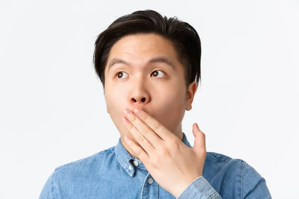 Close-up van geschokt en geschrokken jonge aziatische man hijgend van verbazing, kijken linksboven hoek, dekking geopende mond in ontzag, staan onder de indruk over witte achtergrond — Stockfoto