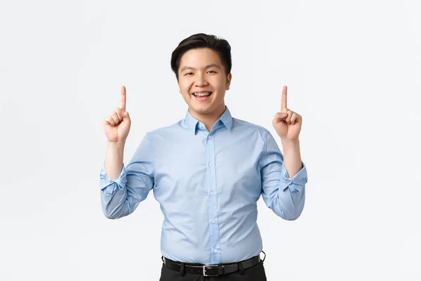 İş, finans ve insan konsepti. İyi görünümlü mavi gömlekli Asyalı bir işadamı, parmaklarını havaya kaldırıp gülümsüyor, mutlu bir şekilde anons yapıyor, satış elemanı ürünü tavsiye ediyor. — Stok fotoğraf