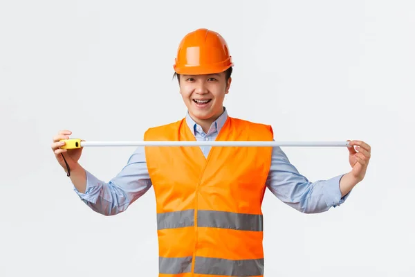 Secteur du bâtiment et concept des travailleurs industriels. Constructeur asiatique enthousiaste confiant, ingénieur en casque et vêtements réfléchissants mesure de robinet ouvert et souriant optimiste, fond blanc — Photo