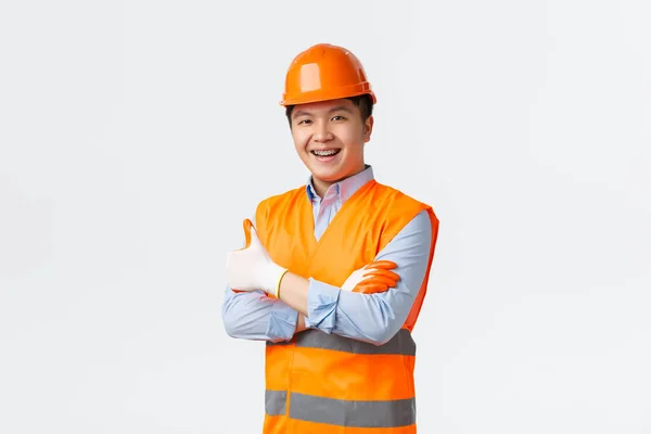 Secteur du bâtiment et concept des travailleurs industriels. Confiant jeune ingénieur asiatique, directeur de la construction en vêtements réfléchissants et casque, bras croisés et souriant, garantir la qualité, fond blanc — Photo