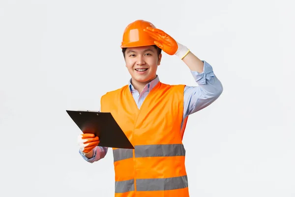 İnşaat sektörü ve endüstriyel işçiler kavramı. Neşeli gülümseyen Asyalı inşaat müdürü, miğferli müfettiş ve güvenlik eldiveni mühendisi, elinde not panosu, izin ver. — Stok fotoğraf