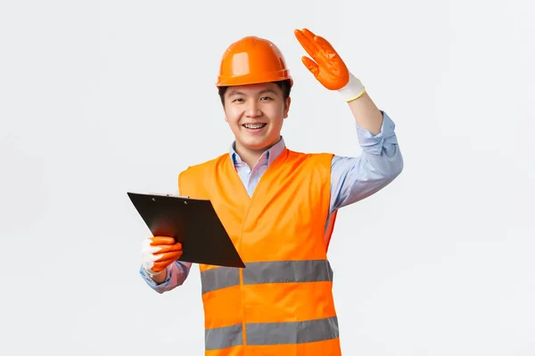 Concepto de sector de la construcción y trabajadores industriales. Alegre sonriente asiático gerente de construcción, inspector en casco y guantes de seguridad saludando ingeniero, sujetando portapapeles, dar permiso — Foto de Stock