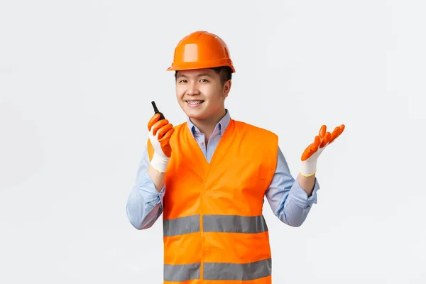 Secteur du bâtiment et concept des travailleurs industriels. Souriant confiant ingénieur en chef asiatique, directeur de la construction donner des ordres via talkie-walkie, regardant avec plaisir à la caméra, porter un casque de sécurité — Photo