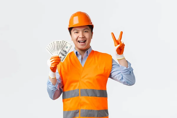 Az építőipar és az ipari dolgozók koncepciója. Boldog mosolygós ázsiai építész, építési vezető sisak és reflektív ruházat mutatja béke jel és a pénz, van fizetés, fehér háttér — Stock Fotó