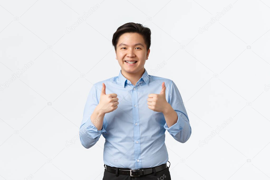 Business, finance and people concept. Upbeat handsome asian male entrepreneur, japanese salesman with braces, showing thumbs-up in approval, recommend service or company