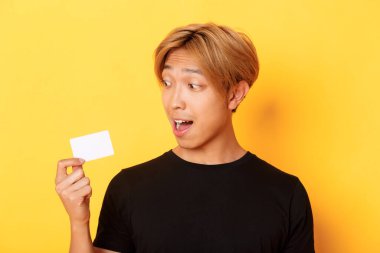 Afallamış Asyalı adamın kredi kartından bahseden yakın plan fotoğrafı, sarı arka planda duruyor.