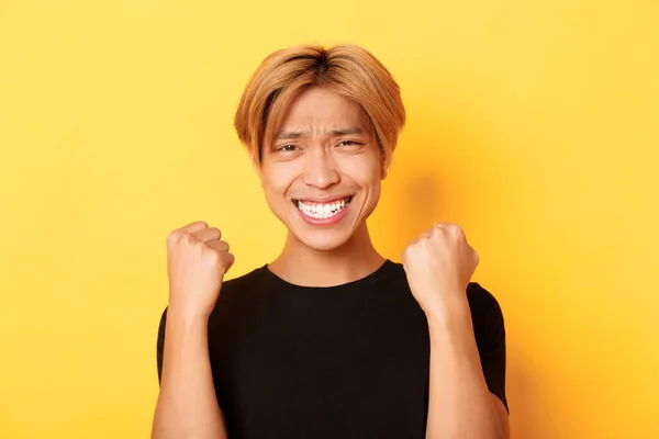 Primer plano de suerte feliz asiático chico ganar premio, haciendo puño bomba gesto y sonriendo satisfecho, triunfando sobre logro, de pie amarillo fondo — Foto de Stock