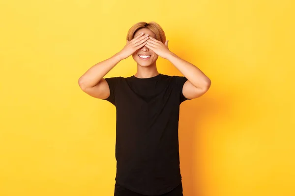 Portrét vzrušeného šťastného asijského chlapa, usmívající se a zavřené oči s rukama, stojící žluté pozadí — Stock fotografie