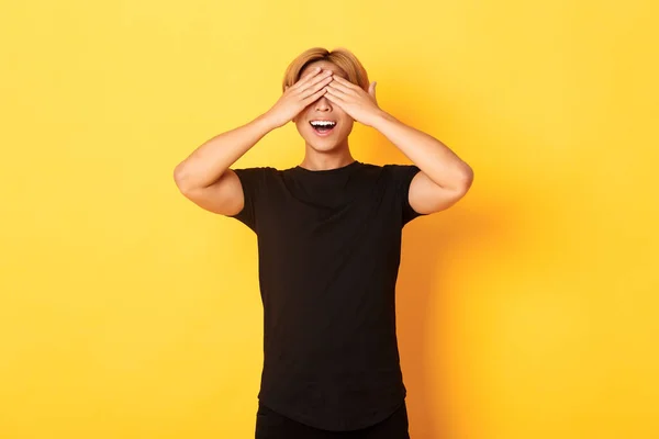 Retrato de tipo rubio divertido y emocionado sonriente cerró los ojos con las palmas, esperando sorpresa, de pie fondo amarillo — Foto de Stock