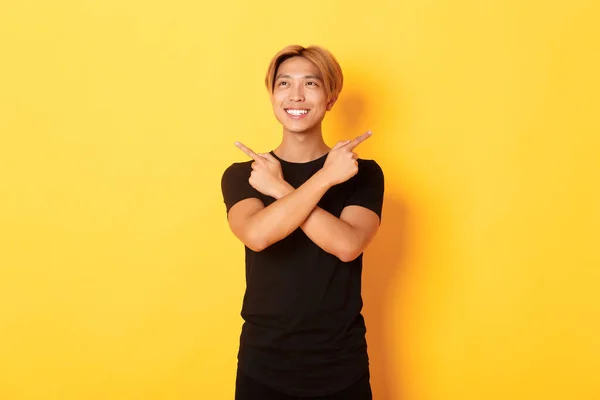 Portré mosolygós elégedett ázsiai srác, balra néz, és döntést hoz, rámutatva oldalra, sárga háttér — Stock Fotó