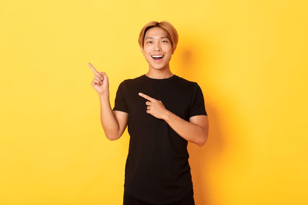 Портрет веселого азіатського чоловіка, який вказує пальці на верхній лівий кут, посміхається і показує банер задоволений, жовтий фон — стокове фото