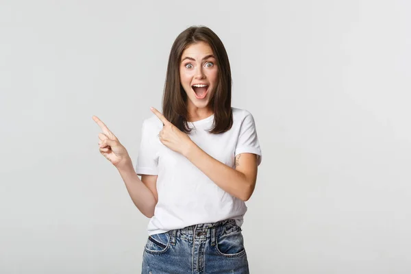 Menina bonita animado sorrindo, apontando os dedos canto superior esquerdo e olhando satisfeito para o logotipo — Fotografia de Stock