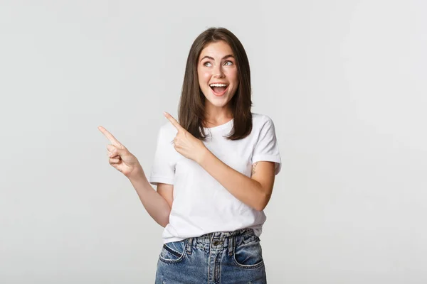 Atraente sorridente morena menina apontando dedos canto superior esquerdo, mostrando logotipo — Fotografia de Stock