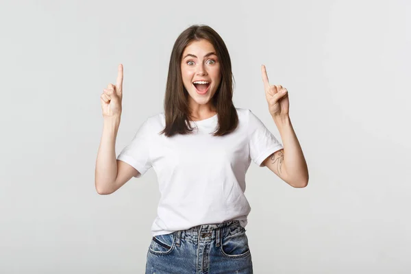 Menina morena sorridente atraente apontando os dedos para cima, mostrando logotipo — Fotografia de Stock