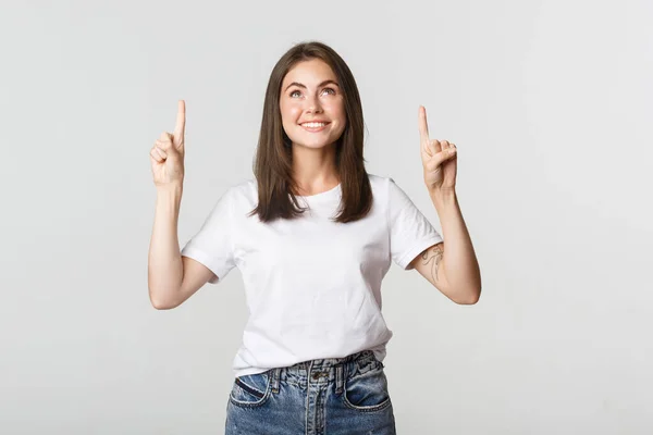 Atractiva chica morena sonriente apuntando con los dedos hacia arriba, mostrando el logotipo — Foto de Stock