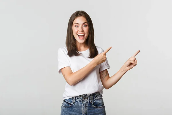 Atraente sorridente morena menina apontando dedos canto superior esquerdo, mostrando logotipo — Fotografia de Stock