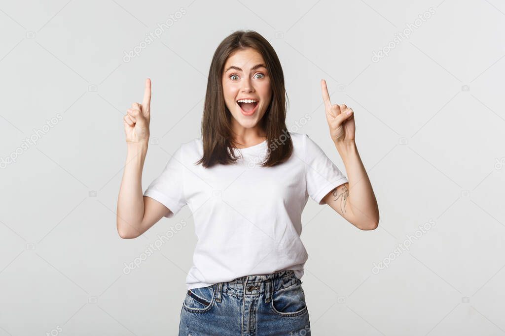 Attractive smiling brunette girl pointing fingers up, showing logo