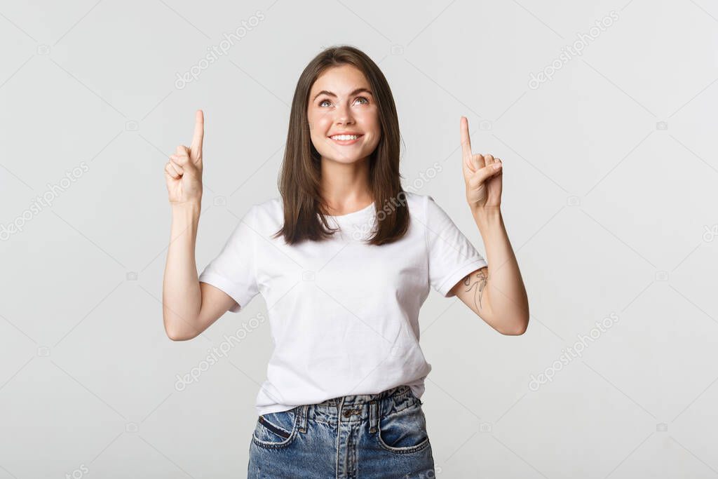 Attractive smiling brunette girl pointing fingers up, showing logo