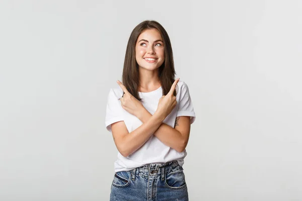 Mujer sonriente reflexiva mirando esquina superior izquierda complacido, señalando los dedos hacia los lados — Foto de Stock