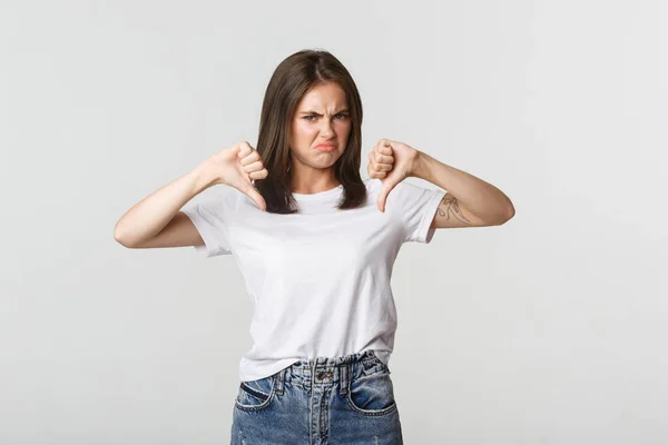 Deluso sorridente ragazza carina mostrando pollici verso il basso, esprimere antipatia — Foto Stock