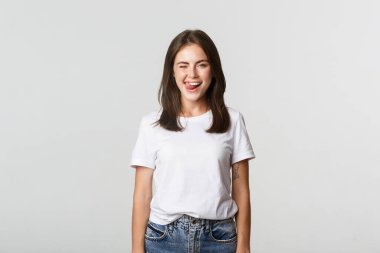 Şımarık, güzel, genç bir kadın göz kırpıyor ve dilinin flört ettiğini gösteriyor.