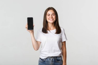 Çekici gülümseyen genç bayan memnun görünüyor, akıllı telefon ekranı gösteriyor.