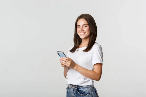 Attraktiv ung brunett kvinna som använder mobiltelefon och ler mot kameran — Stockfoto