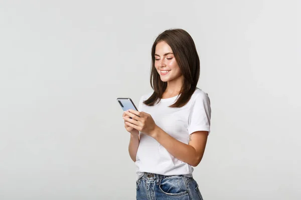 Güzel, gülümseyen bir kız cep telefonu kullanıyor, akıllı telefona bakıyor.