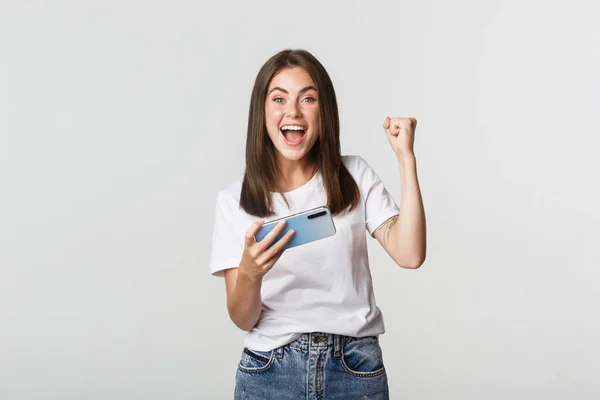 Attraktiv glad brunett flicka vinna i mobilspel, hålla smartphone och glädje — Stockfoto