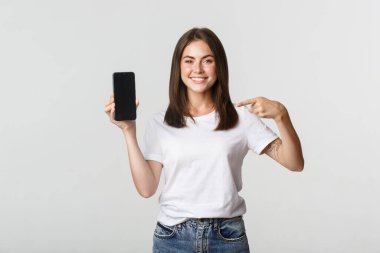 Çekici, gülümseyen bir kadın akıllı telefon ekranını işaret ediyor.